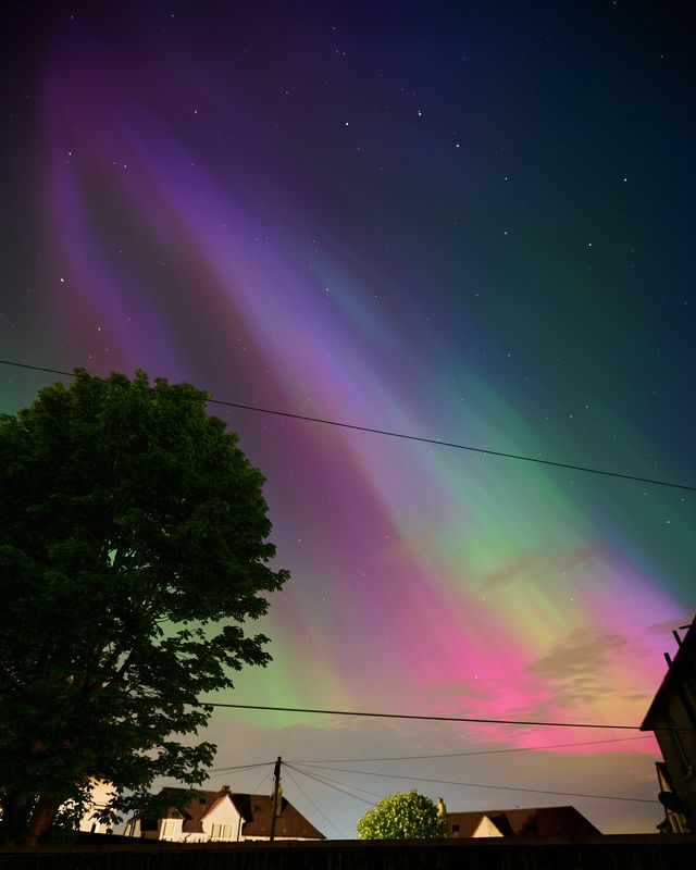 Very colourful aurora in the western sky above houses.